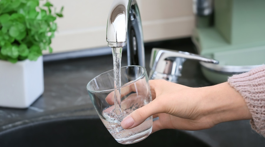 Hand holding a glass under a kitchen faucet with clean water flowing, emphasizing the importance of backflow prevention for maintaining potable water safety.