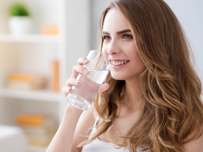 Woman drinking a glass of water, emphasizing the importance of clean water and backflow prevention for public health and safety.