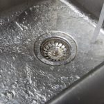 Water flowing into a stainless steel sink with a visible drain, illustrating effective drainage and plumbing maintenance.